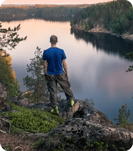 A man standing on top of a rock overlooking water.