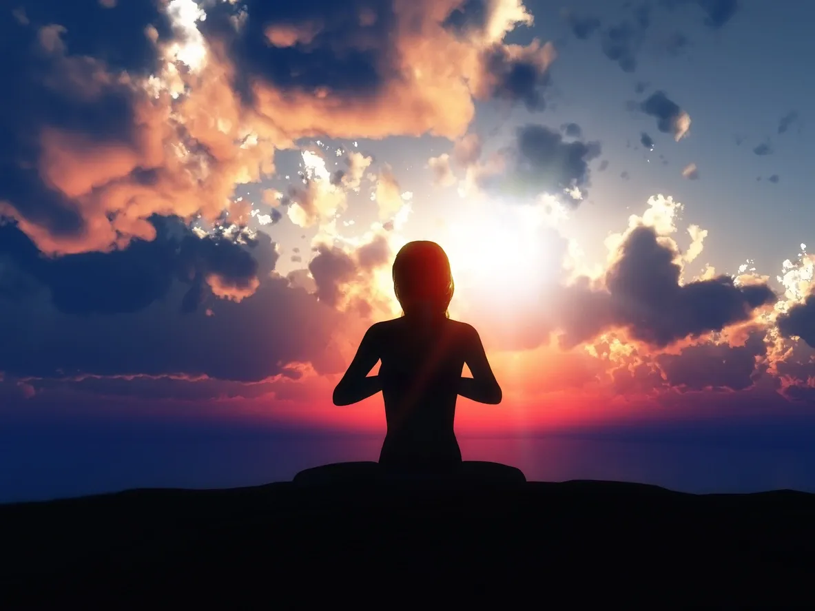 A person sitting in the sunset with their hands up.